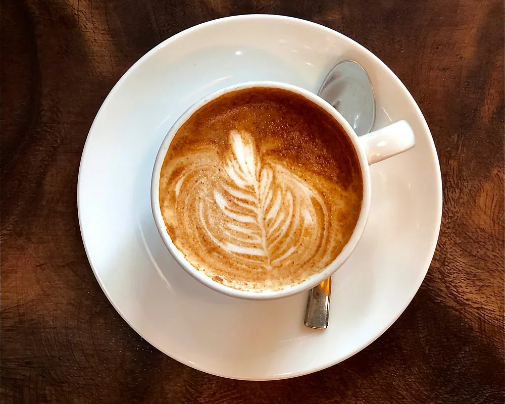 Latte with rosetta art being placed on a wooden counter